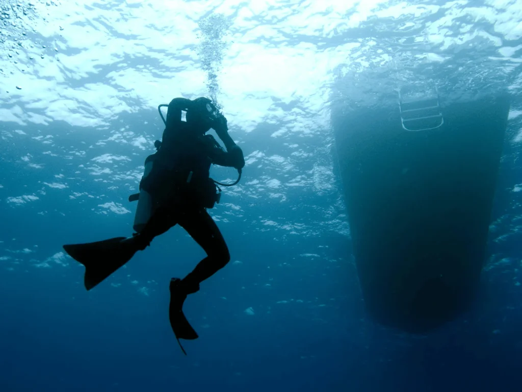 Diver tilting head upward and exhaling through nose to push water out of scuba mask.